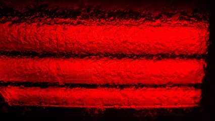 Red light shines through ice, creating a textured surface with lines and reflections in a dark setting during the night