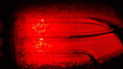 Bright red car light shows through frost on a cold winter night in a parking lot
