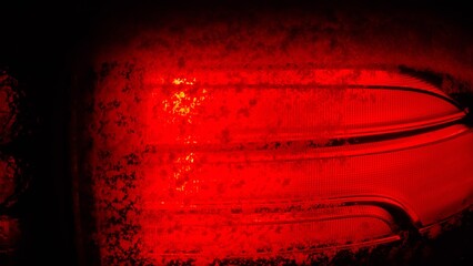 Bright red light shines from a car's taillight at night showing the detail of the lens and lenses