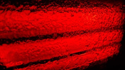 Light shines through a wet glass, creating a red pattern in a dark space during nighttime