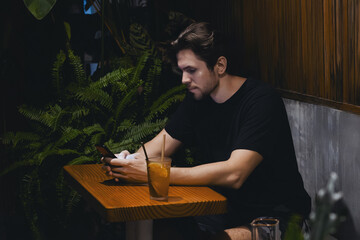Adult caucasian male at cozy cafe with smartphone and iced drink in relaxed setting