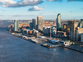 Obraz premium Aerial view of Liverpool at sunrise along the River Mersey, Royal Liver Building, Museum of Liverpool, West Tower, ferries, piers, brick warehouses, sleek glass architecture.