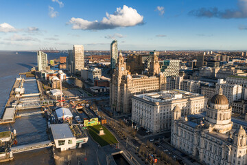 Fototapeta premium Aerial sunrise shows Liverpool waterfront, the Three Graces at Pier Head, River Mersey at left, modern towers, Museum of Liverpool, docks and promenades in warm light.