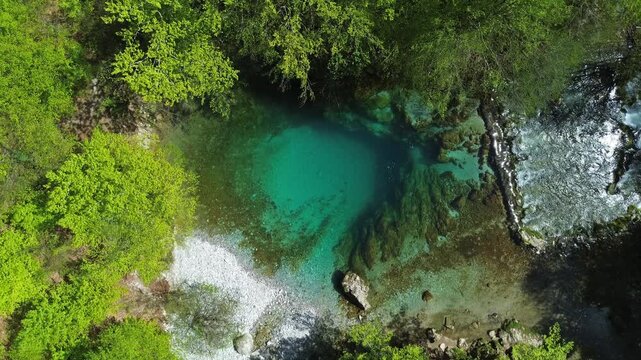 Aerial top view of turquoise spring water surrounded by lush green forest, Oko Skakavice in Montenegro, 4k