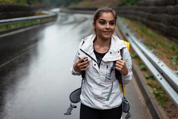 Young woman with backpack walking on a wet road during a rainy day