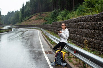 Young woman with backpack checking her phone on a wet mountain road