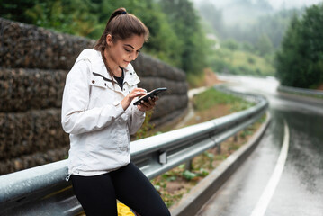 Young woman in sportswear using smartphone on a wet mountain road