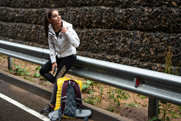 Young woman in sportswear resting by the roadside with a backpack and phone