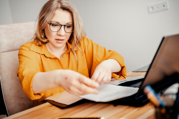 Woman finance consultant reviewing documents with laptop in home office. Tax reporting and financial analysis workflow.