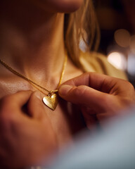 Man fastens heart necklace on woman's neck during dinner