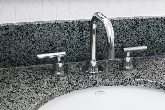 Modern bathroom sink faucet closeup. Chrome tap on granite countertop. Clean washbasin detail. Home interior hygiene concept. Water fixture design. Minimal bathroom equipment.