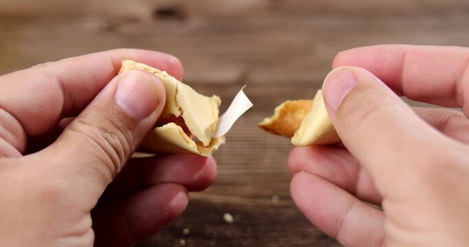 Close up of human hands opening a crunchy Chinese fortune cookie on a dark wooden table background for luck and destiny concepts.