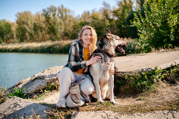 Woman hugging East European Shepherd dog outdoors near water, autumn day, strong human pet...