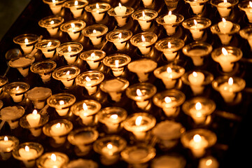 Rows of burning white votive candles in glass holders casting a