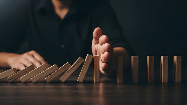In this close-up, a focused individual skillfully prevents a chain reaction of falling dominoes, symbolizing proactive risk management and stability.