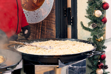 Chef stirring creamy K&auml;sesp&auml;tzle in a large pan at a festive o