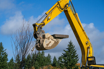 Excavator bucket attachment moving section of asphalt cut out of road to dig a utilities trench, public infrastructure construction site
