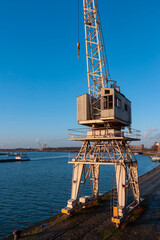Historic harbor crane on waterfront with operator cabin and blue water backdrop