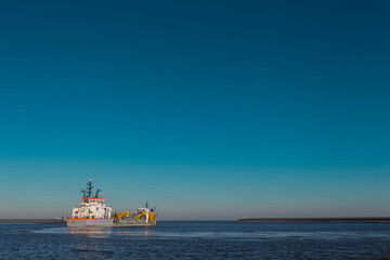 Fototapeta premium White and yellow dredging vessel working at sea under clear blue sky