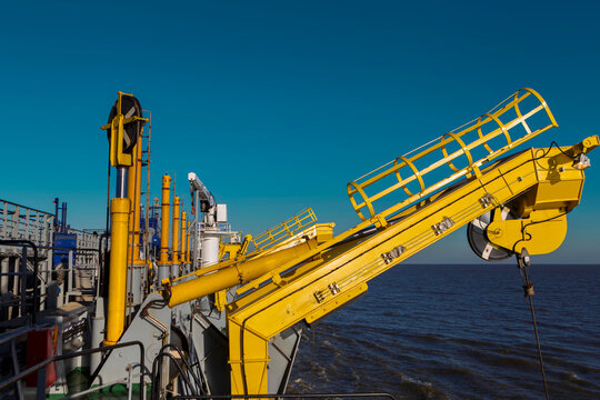 Yellow hydraulic crane with lattice boom mounted on dredging vessel deck