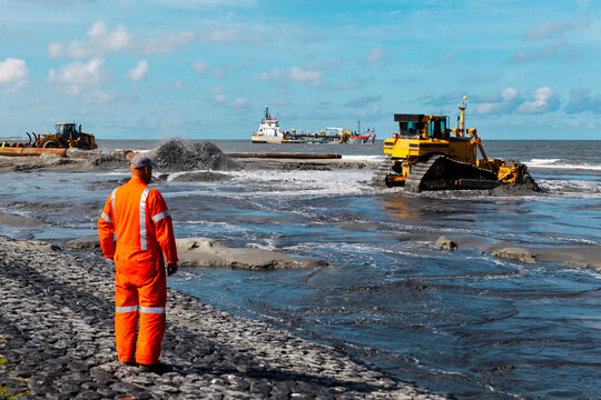 Safety worker overseeing beach nourishment with heavy equipment and dredging vessel