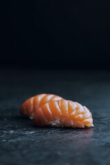 Minimalist image of two fresh salmon nigiri pieces on a dark stone surface, perfect for sushi menus, ads, or food banners.
