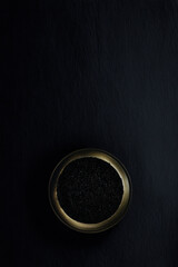 Luxury black caviar in metal bowl on dark background, copy space on top.
