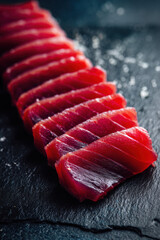 Close-up of fresh, vibrant red tuna sashimi slices arranged neatly on a textured dark slate surface, ready for gourmet presentation.
