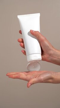 Vertical video of female hands opening white mockup tube and applying gel cream to palm of their hand on beige background. Concept of hydrating cream for freshness, rejuvenation, and beauty ritual