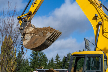 Excavator bucket attachment up high carrying dirt, public infrastructure construction site
