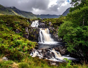 Cascade tumbles amidst green hills, with moody sky & trees framing water's flow