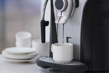 Electric espresso machine making coffee, plates and cups on white table indoors, closeup. Space for text