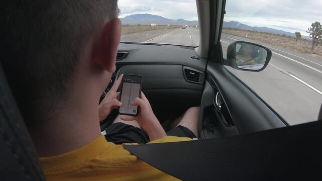 Young man on the passenger seat checking the directions on a map on smartphone, traveling around the Nevada desert, towards Los Angeles. Friends roadtrip concept