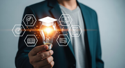A man holds a glowing light bulb adorned with a graduation cap and surrounded by education symbols. He is in business suite, representing innovation, ideas and learning.