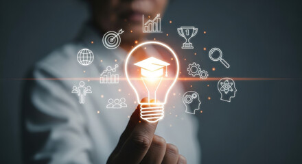 Close-up shot of a woman's hand gently touching a glowing light bulb icon with a graduation cap inside, encircled by business symbols, against a dark backdrop.