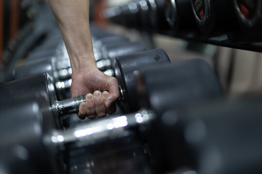 Close-up of a hand gripping a dumbbell from a rack at the gym, representing strength training, physical fitness, and workout motivation with focus on effort determination.
