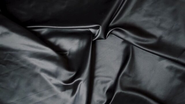 Close-up of a smooth, dark gray satin fabric with folds and creases on a white background.