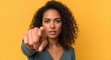 Woman with Curly Hair Pointing Directly at Viewer Against Vibrant Yellow Background