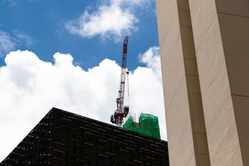 Crane and building under construction against sky is covered with white clouds white in background. Builders work on large construction site and there are many cranes working in field of new.
