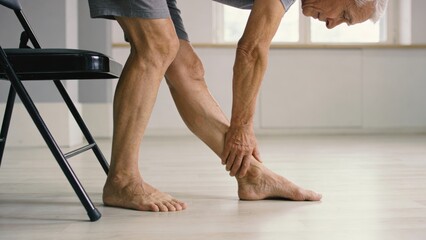 Senior stretching leg while seated on a chair, active aging concept