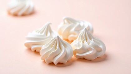Close-up of four swirled white pastries on a pale pink surface, with a blurred one