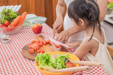 Asian pregnant woman cooking healthy salad with preschool little girl daughter in kitchen, bonding relationship mother and child spend time together preparing food for breakfast, lifestyle motherhood