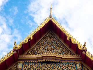 Fototapeta premium Beautiful golden gable apex on roof of Thai buddhist temple against blue sky and clouds, traditional art architecture and religion concept.