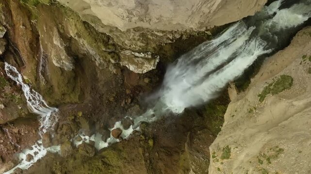 An aerial drone shot captures the stunning Sig&ouml;ldufoss waterfall flowing into a river in the Icelandic Highlands. The powerful water cascades over the rugged, moss-covered cliffside, showcasing the ra