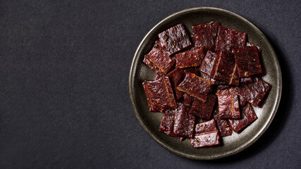 flat lay pile of jerky pork in bowl on black background with copy space