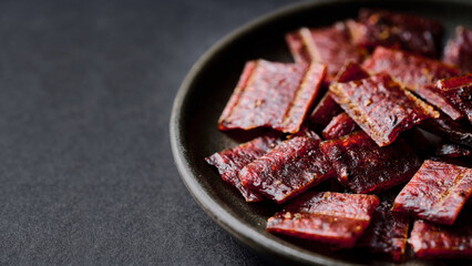 closeup pile of jerky pork in bowl on black background with copy space