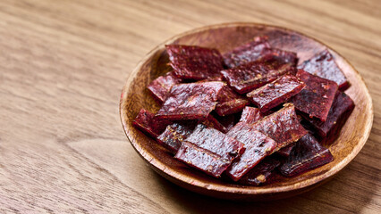 closeup pile of jerky pork in bowl on wood background with copy space