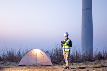 An Asian male engineer working  with digital tablet at a wind farm on the mountain