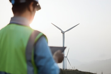 An Asian male engineer working  with digital tablet at a wind farm on the mountain