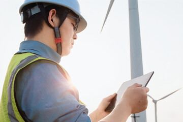 An Asian male engineer working  with digital tablet at a wind farm on the mountain